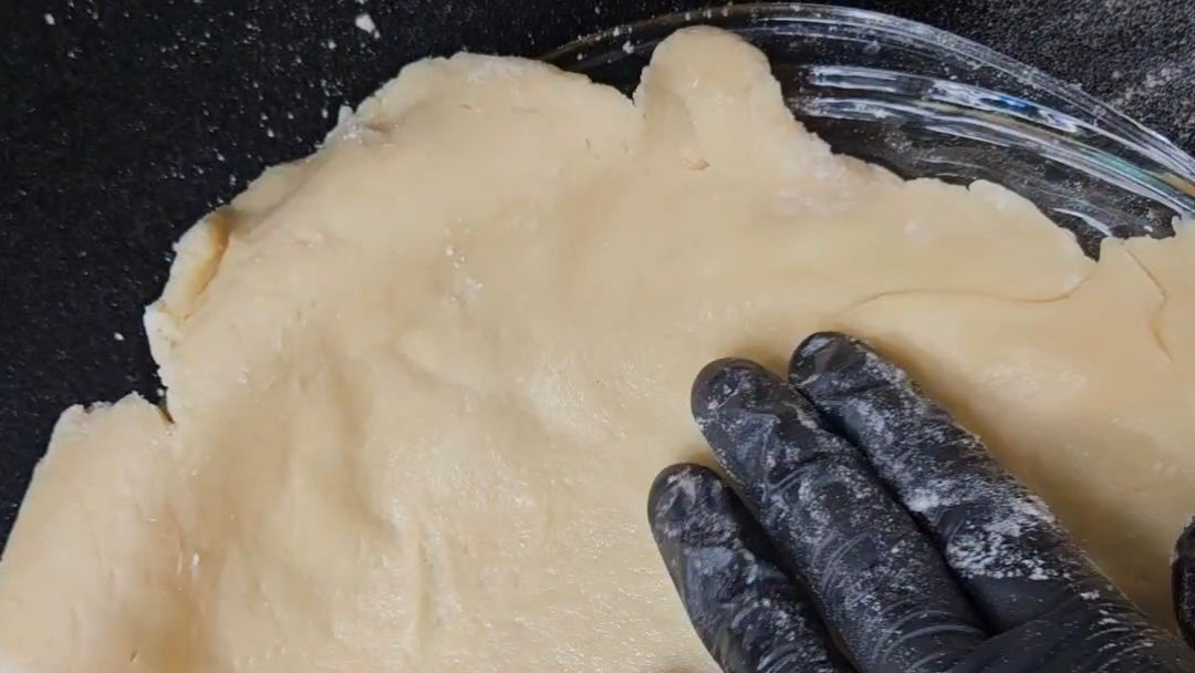 Hand wearing a black glove shaping dough in a pie dish on a dark surface
