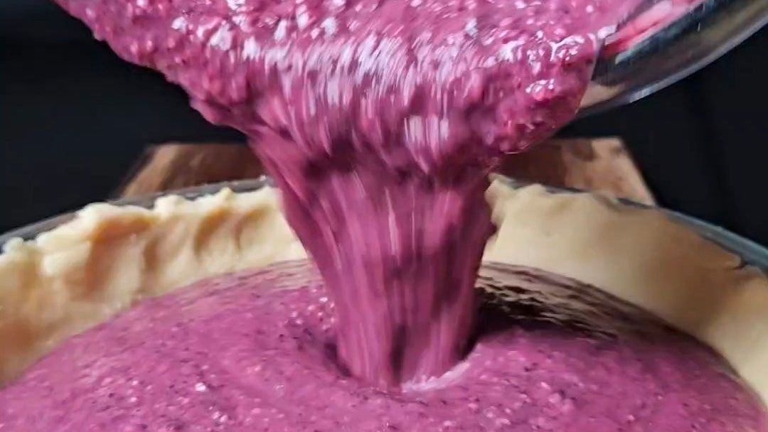 Purple pie filling being poured into a pie crust